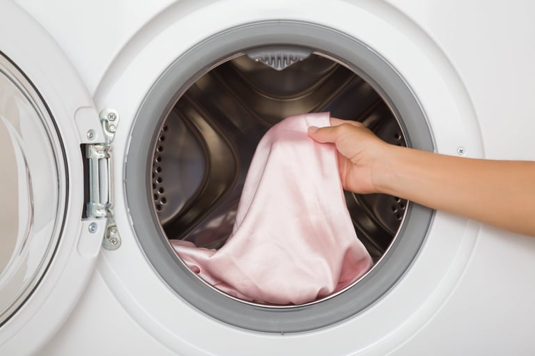 Young adult woman hands holding and unloading pink silk fabric from opened white washing machine