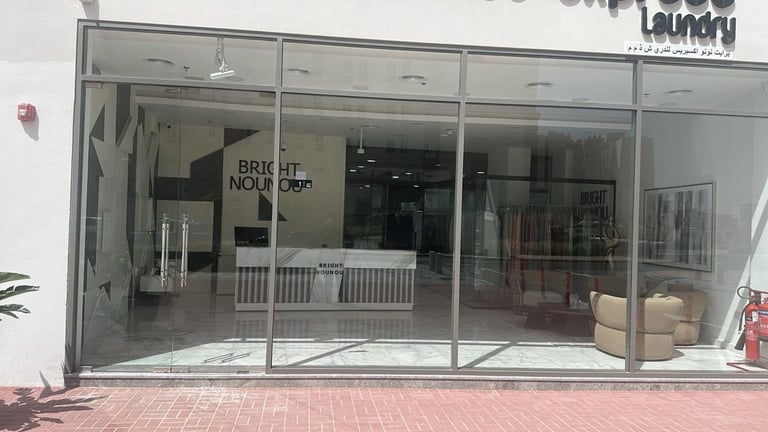 Empty storefront with large glass windows and white frame, brick exterior, closed laundry shop with signage visible inside